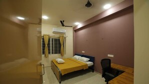 A bedroom with a bed, a desk, a chair, an air conditioner, and a window with curtains. - Perambalur Villa  (Perambalūr)