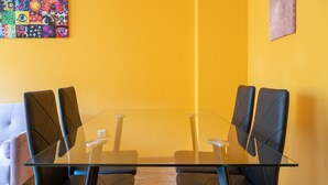 Un salón de conferencias con una mesa de vidrio y cuatro sillas negras, un sofá rosa, y un cuadro abstracto colorido en la pared.