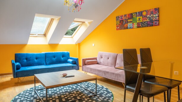 Una sala de estar moderna con un sofá azul, un sofá rosa, una mesa de comedor de vidrio y una araña.