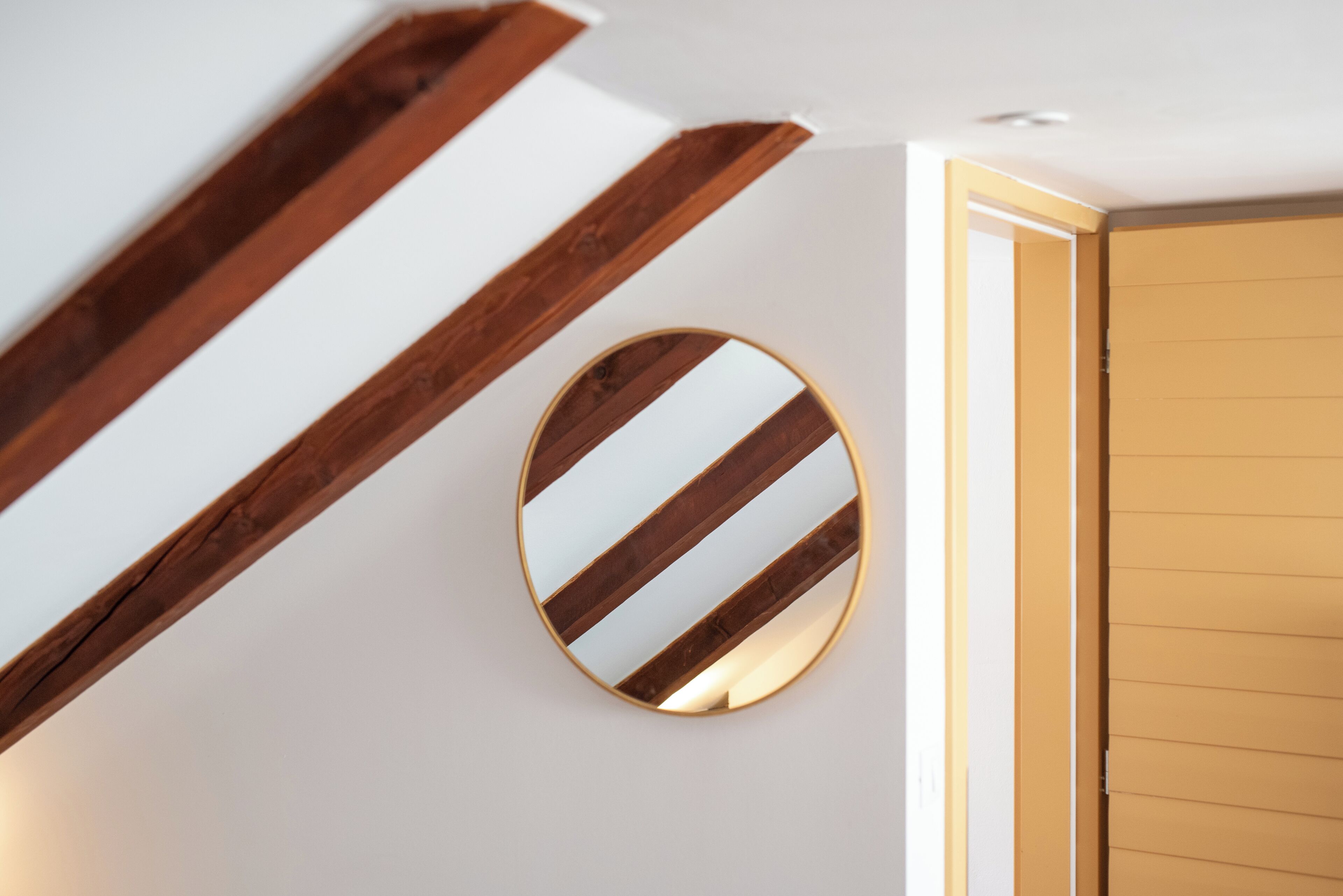 Ein Holzbalkenbau, ein runder Spiegel mit diagonalen Streifen und eine Holztür.