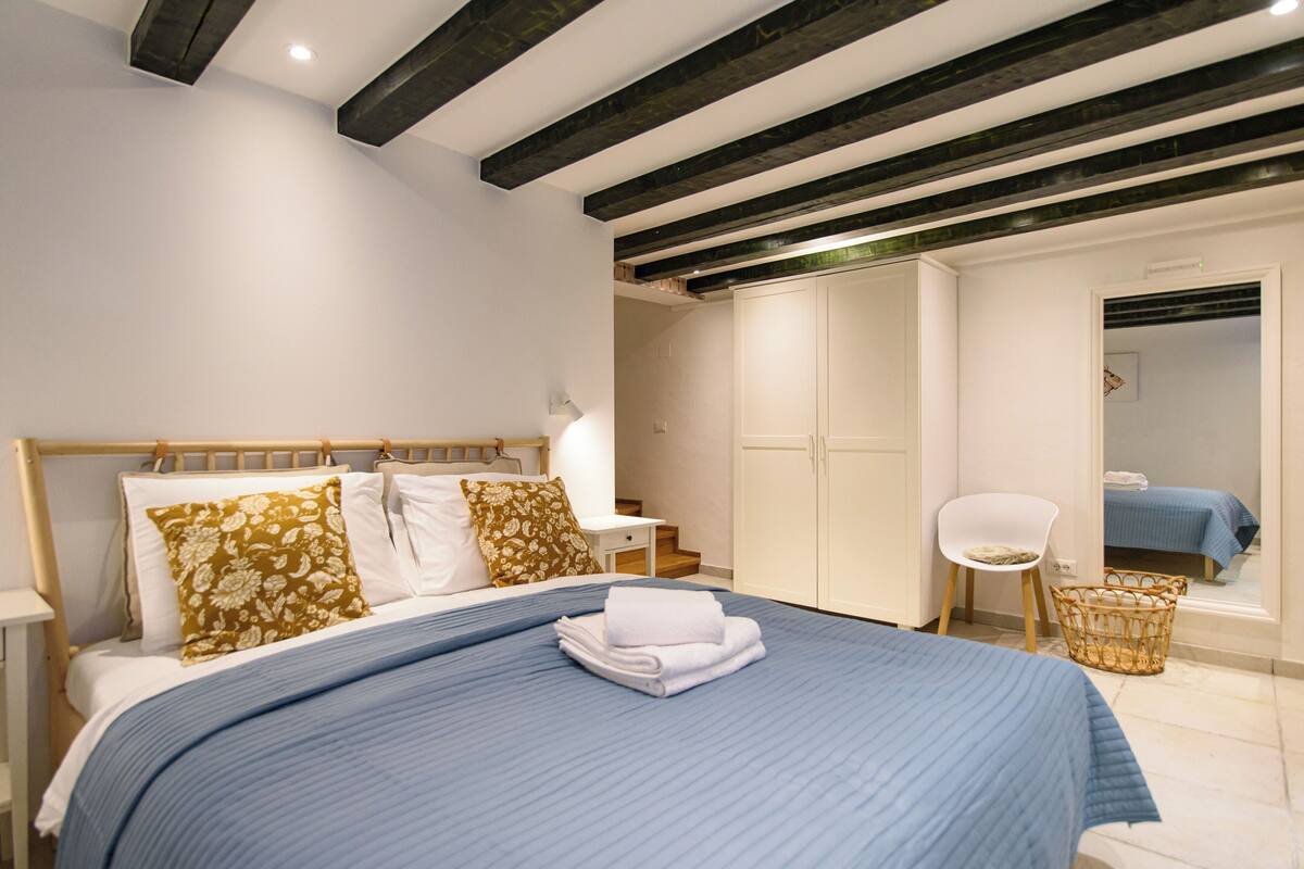 Un dormitorio con cama, una silla, un armario y un espejo.