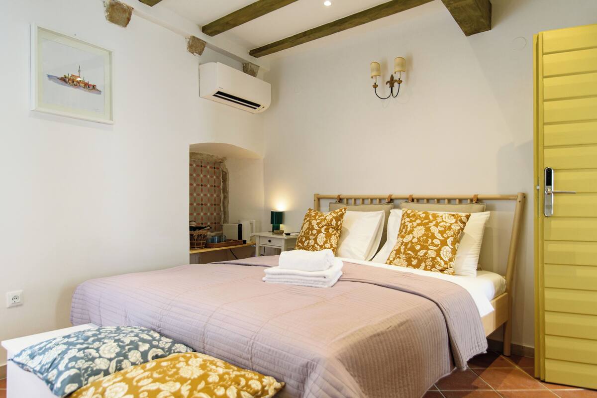 Un dormitorio con cama, mesita de noche, aire acondicionado, lámpara de pared y puerta.