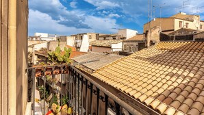 A residential area with terracotta-tiled rooftops, a metal balcony railing, and a clear sky.