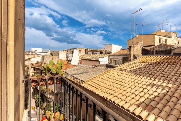A residential area with terracotta-tiled rooftops, a metal balcony railing, and a clear sky.