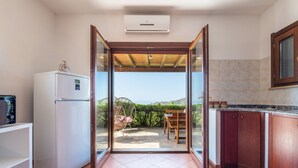 Une cuisine équipée d’un réfrigérateur, de placards et donnant sur une terrasse extérieure grâce à une porte vitrée.
