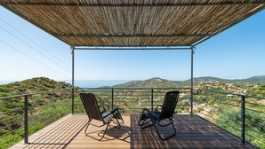 Une terrasse avec deux chaises, une terrasse en bois, une rambarde en métal et une vue sur des collines lointaines et la mer.