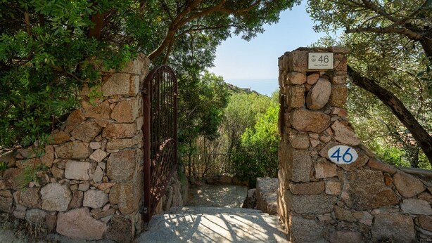 Une porte en pierre ornée d’un symbole « # », qui mène à un sentier bordé de verdure.