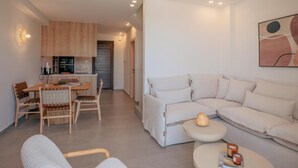 A modern living room with a sofa, a dining table, and chairs. There is a kitchen area with cabinets and a microwave. - Villa Carob, Aesthete Villas (Rethymno)