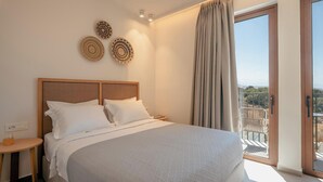 A hotel room with a large bed, a bedside table, a wall-mounted light, and a view of a balcony. - Villa Carob, Aesthete Villas (Rethymno)