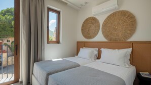 A hotel room with two beds, a large window with curtains, an air conditioning unit, and two woven wall decorations. - Villa Carob, Aesthete Villas (Rethymno)