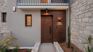 A modern building with a stone facade, a wooden door, and a small balcony with a railing. - Villa Carob, Aesthete Villas (Rethymno)