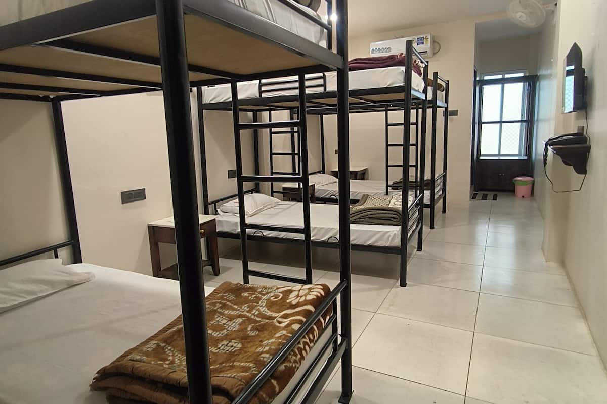 A dormitory room with bunk beds, a small table, and a wall-mounted heater.