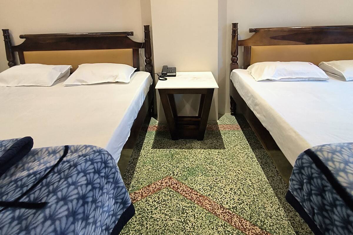 A hotel room with two beds, a small table, and a painting of flowers on the wall.