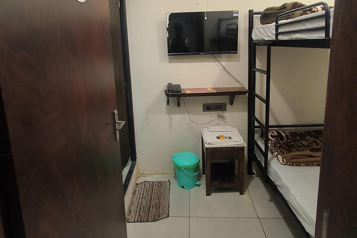 A compact room with a bunk bed, a small desk, a television mounted on the wall, and a ceiling fan.