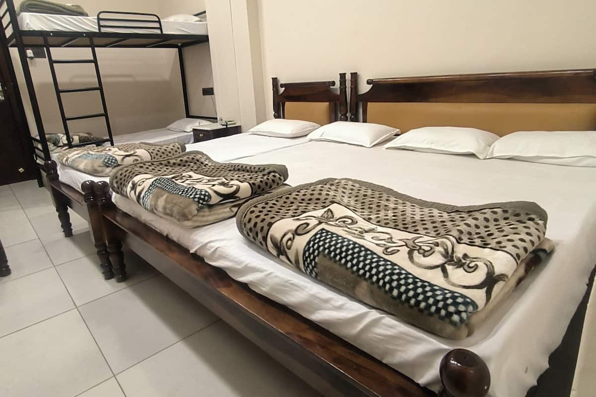 A single bed with a wooden headboard and a patterned blanket. A bunk bed is visible in the background.