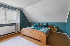 A bedroom with a sloped ceiling, a wooden bed, a window with curtains, and a radiator. - Apartment 'Family Küstenbrise' with Wi-Fi (Heide)