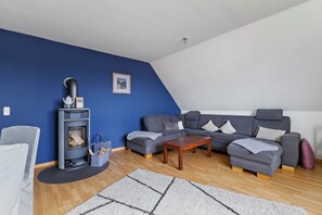 A living room with a sofa, a coffee table, a fireplace, and a blue wall. - Apartment 'Family Küstenbrise' with Wi-Fi (Heide)