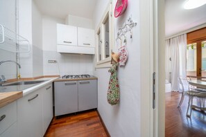 Eine kleine Küche mit weißen Schränken, einer Holz Arbeitsplatte und einem kleinen Fenster.