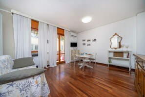 Una sala de estar con un sofá, una mesa de comedor con sillas, un televisor y un espejo.