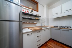 Una cocina moderna con armarios blancos, un refrigerador de acero inoxidable, una encimera de madera y un lavamanos integrado.