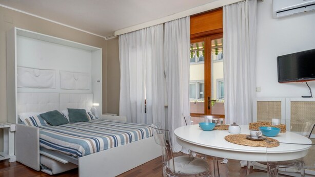 A modern room with a bed, a dining table, and a TV. - GuestHost - Cozy 53 sqm apartment, perfect for four people, located on the first floor of a building with an elevator (NOT accessible to disabled guests).The property is located in Grado, known as the Island of the Sun, a beautiful lagoon town famous for (Grago GO)