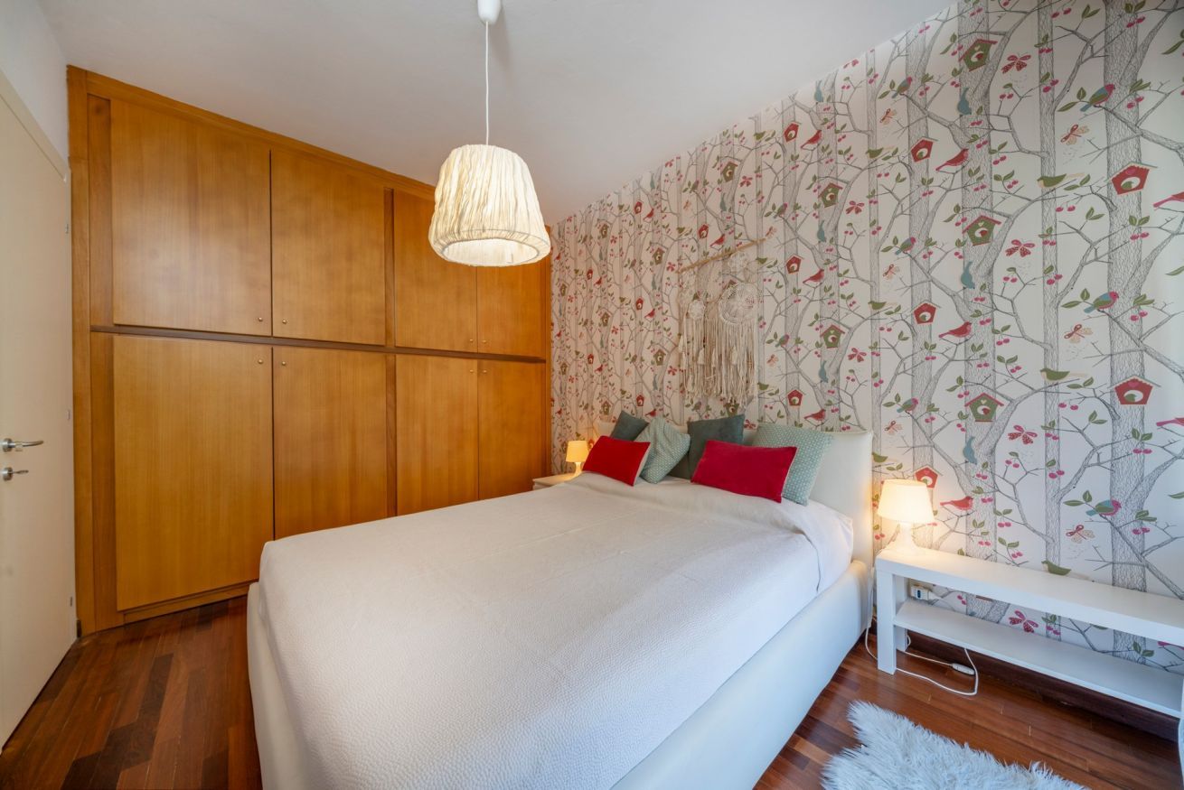 A bedroom with a large bed, wooden wardrobe, and floral wallpaper.