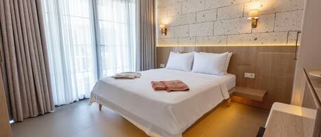 Una habitación de hotel moderna con una cama grande, dos mesitas de noche, una pared de acento de piedra y un ventanal con cortinas.