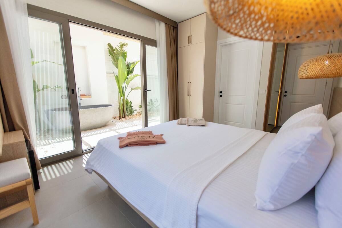 A bedroom with a large bed, a sliding glass door to a balcony, a wardrobe, and a hanging light fixture.
