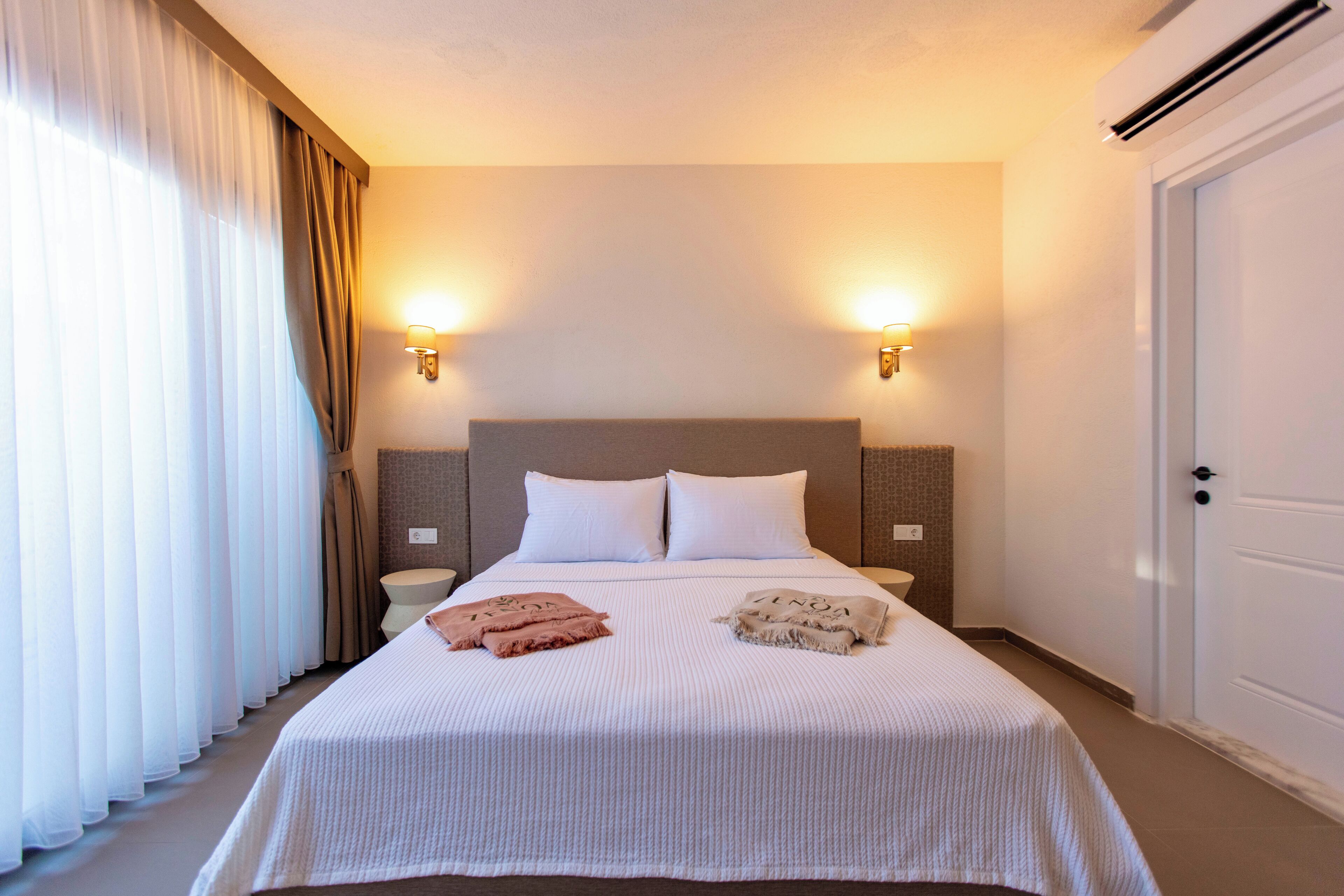 A hotel room with a large bed, two bedside lamps, a nightstand, and a door.