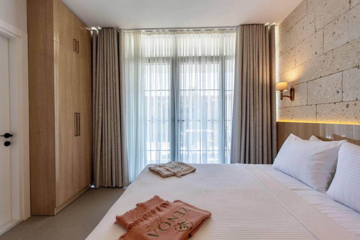 A hotel room with a large bed, wooden wardrobe, and a stone wall.