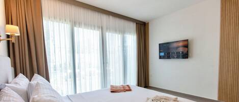 Une chambre d’hôtel avec un grand lit, un téléviseur à écran plat et une fenêtre avec des rideaux.