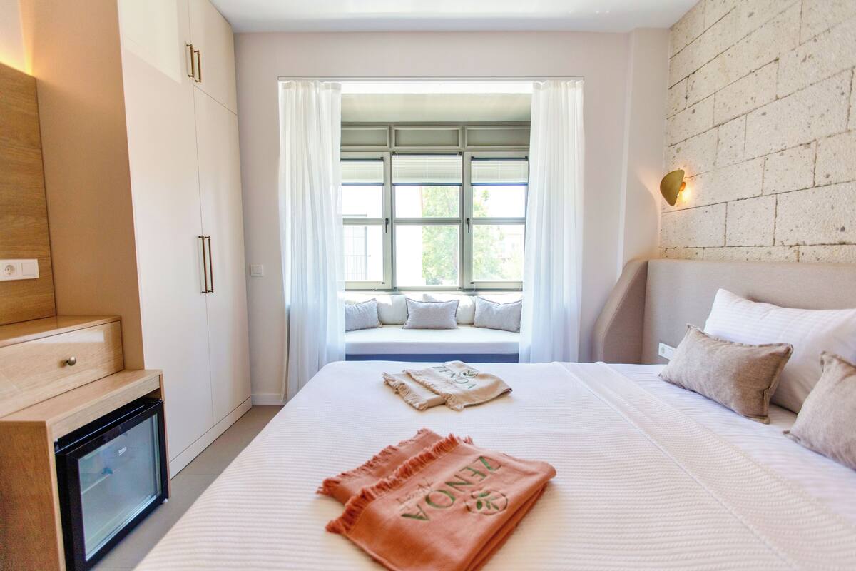 A bedroom with a bed, a nightstand, a built-in TV, a window with curtains, and a brick wall.