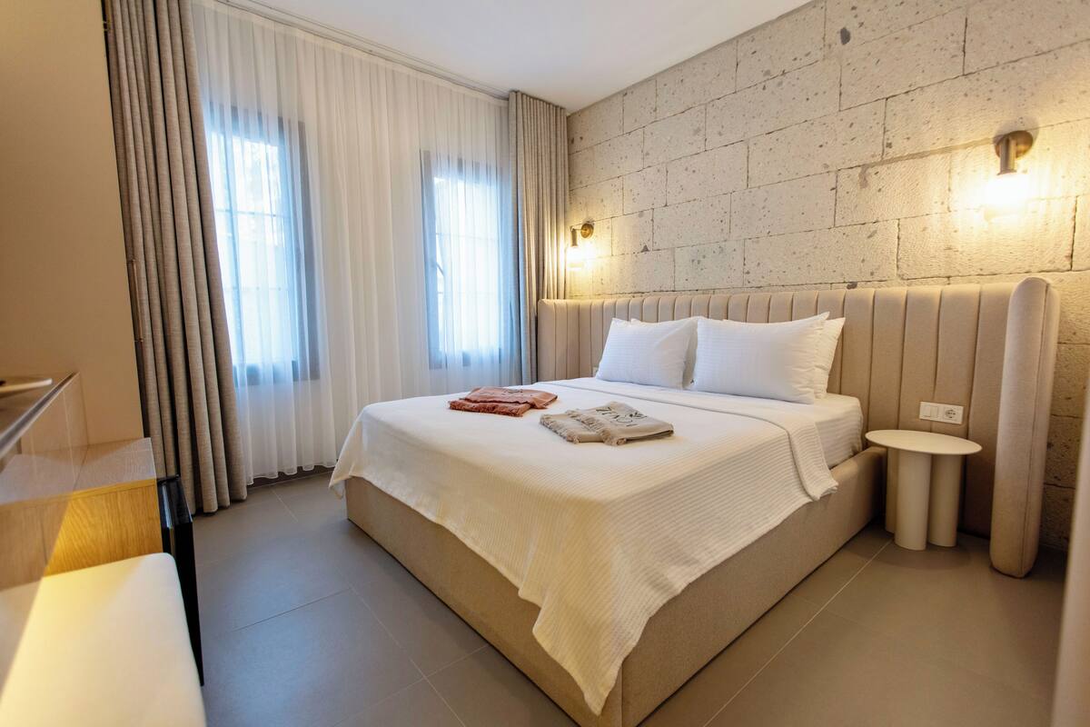 A hotel room with a large bed, a bedside table, and a wall-mounted light fixture.