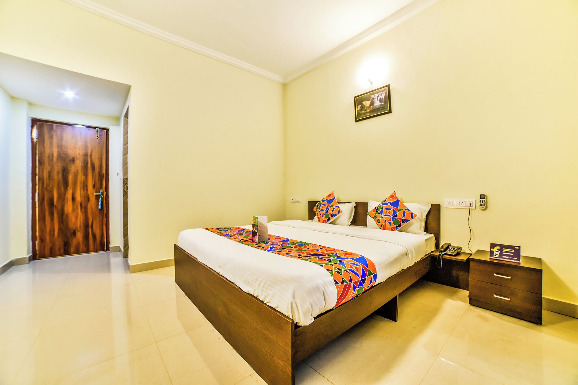 Habitación de hotel con una cama grande, una mesita de noche, un teléfono en la pared y una puerta.