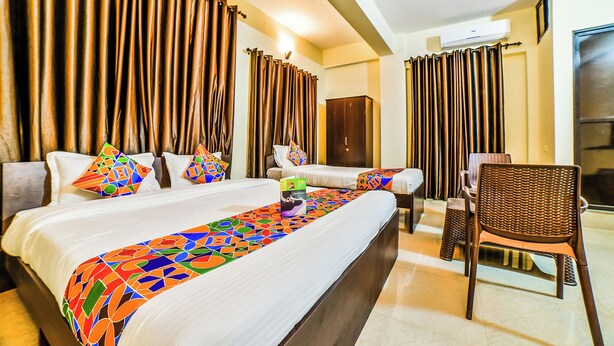 Habitación de hotel con dos camas, un armario, una silla y un ventanal grande con cortinas.