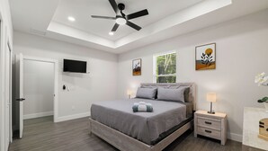 Une chambre à coucher moderne, avec un lit, des tables de chevet, un ventilateur de plafond et des œuvres d’art accrochées aux murs.