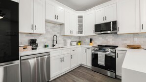 Une cuisine moderne avec des meubles blancs, un lave-vaisselle en acier inoxydable, un four à micro-ondes et une cuisinière.
