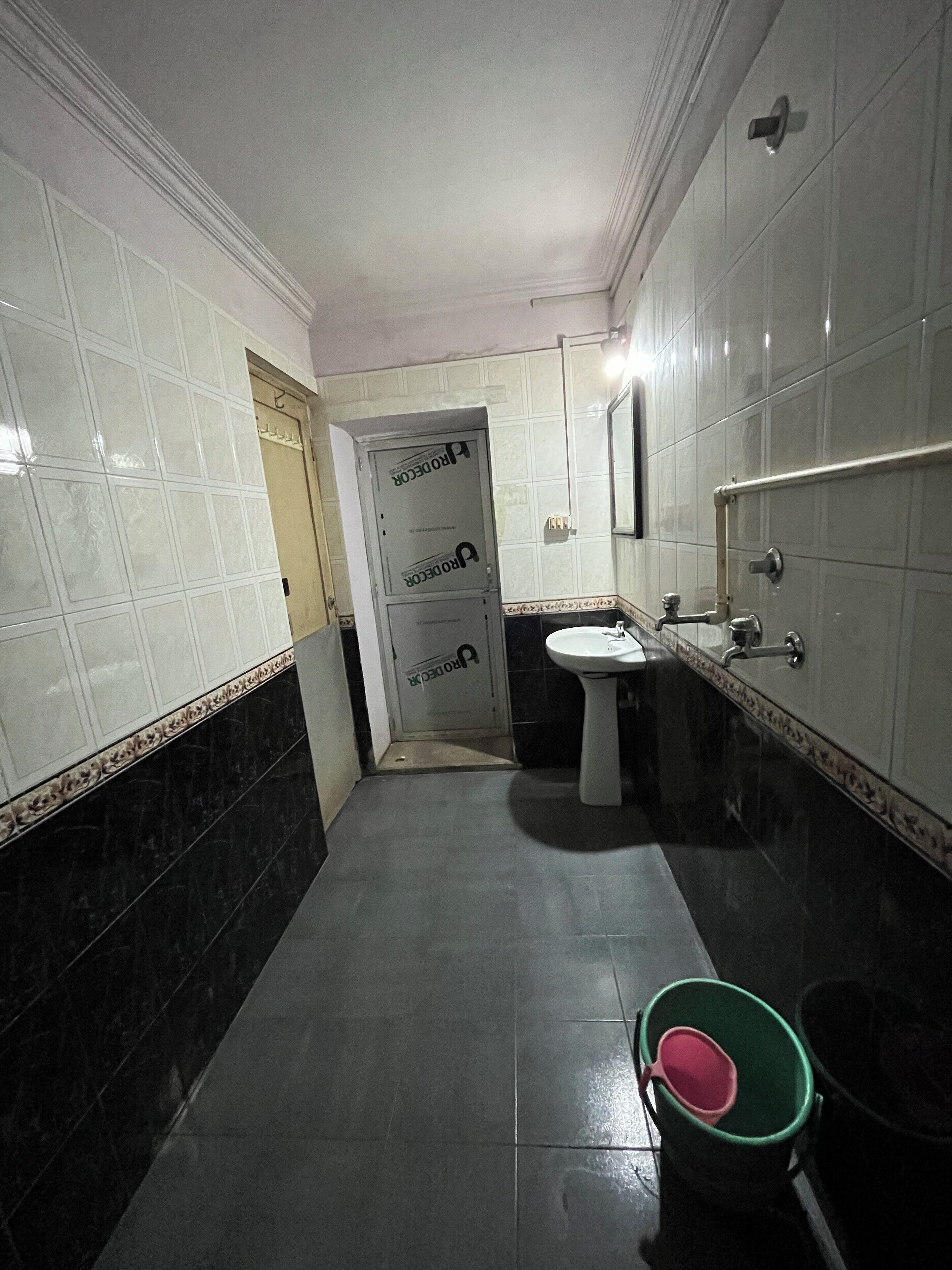 A bathroom with white tiled walls, a pedestal sink, and a green bucket.