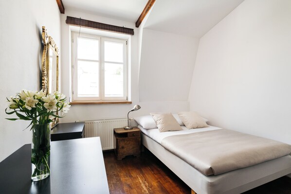 A bedroom with a bed, a nightstand, a lamp, a window, and a vase with flowers.