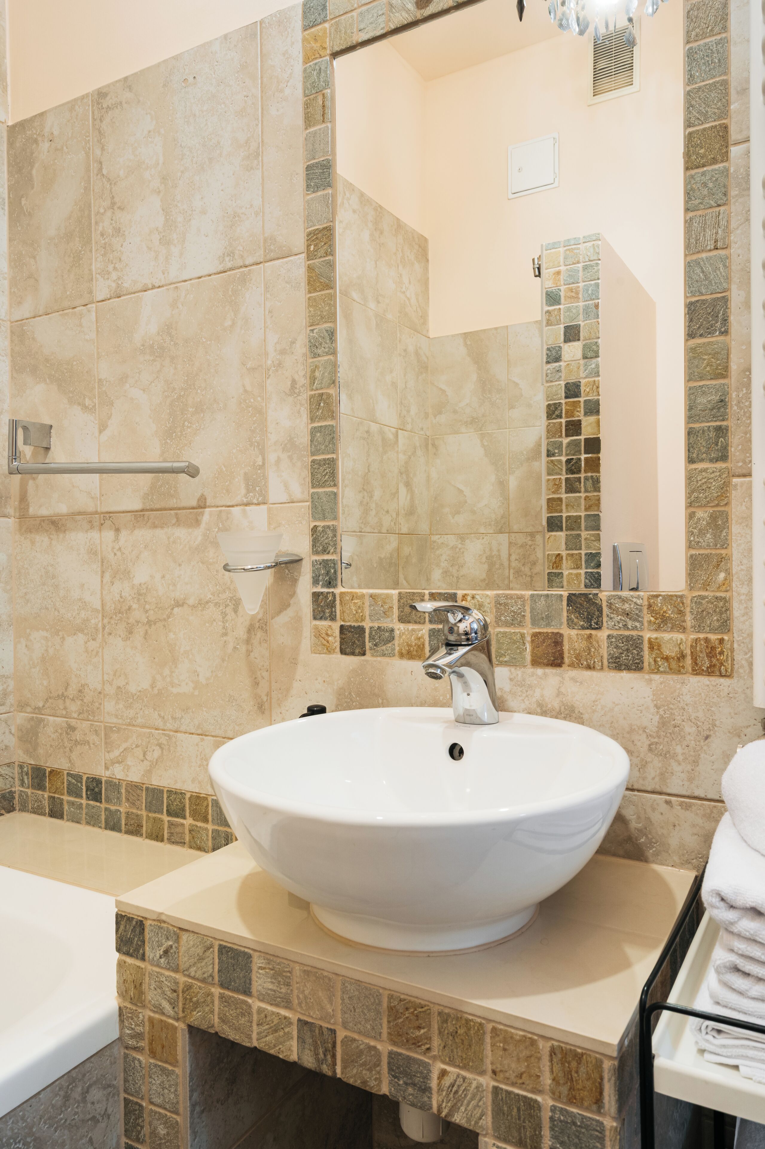 Un baño con un lavabo grande blanco, un espejo y paredes con azulejos.