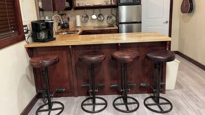 Una cocina con una isla de madera, cuatro taburetes, un refrigerador, un microondas y una guitarra colgada en la pared.