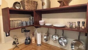 Una cocina con estantes de madera que sostienen diferentes utensilios, una cafetera y ollas colgantes.