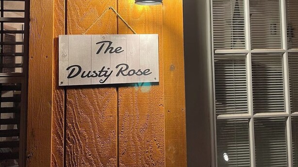 Una puerta de madera con un letrero que dice "The Dusty Rose" y un farol de pared.