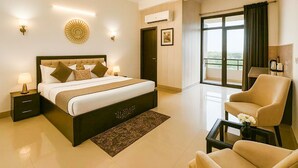 A modern hotel room with a large bed, a sitting area with a chair, a small table, and a view of the outdoors.