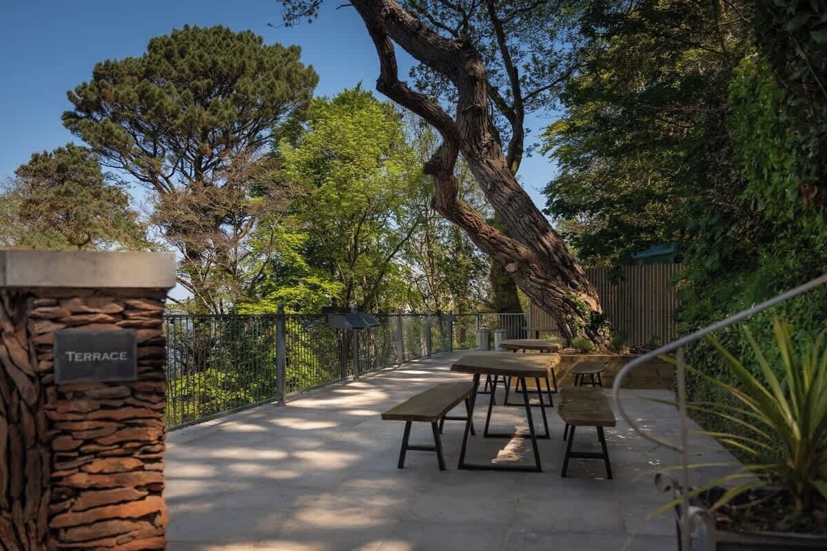 Una terrassa a l'exterior amb columnes de pedra, una tanca metàl·lica i diverses taules i bancs de fusta.