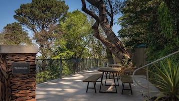 Una terrassa a l'exterior amb columnes de pedra, una tanca metàl·lica i diverses taules i bancs de fusta.