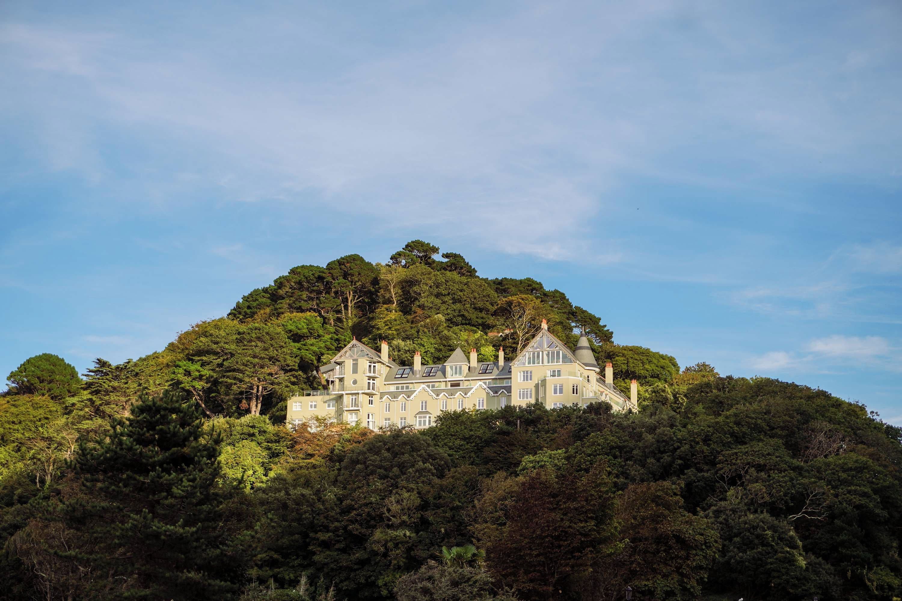 A large, multi-story building with a complex roofline, surrounded by dense forest.