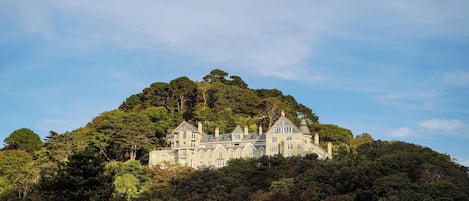 A large, multi-story building with a complex roofline, surrounded by dense forest.