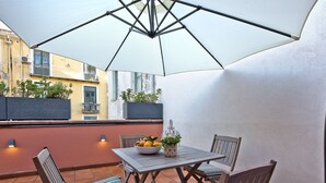 Un patio exterior con una mesa, sillas, un paraguas grande y un frutero.