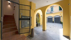 Entrada de un edificio con una escalera, una puerta metálica y un corredor abovedado que conduce a un patio con garaje.